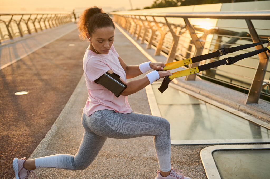 Ćwiczenia wysportowanej zawodniczki z pasami do zawieszania podczas treningu siłowego w środowisku miejskim mostu miejskiego. Całe ciało lekkoatletka w stroju sportowym ciągnąca liny zawieszenia i lonżująca