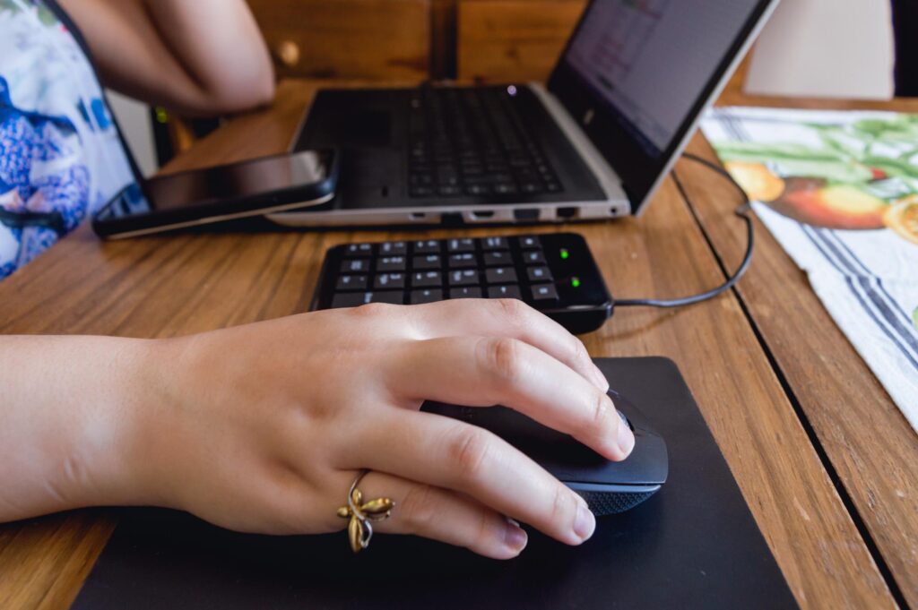 Kaukaska ręka kobiety na myszy obok laptopa na stole