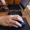 Kaukaska ręka kobiety na myszy obok laptopa na stole