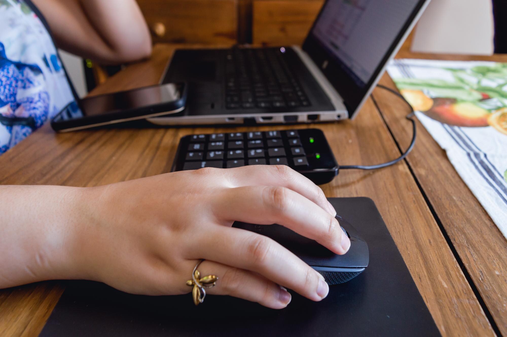 Kaukaska ręka kobiety na myszy obok laptopa na stole
