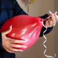 Zbliżenie rąk kobiety wiążącej wstążkę na czerwonym balonie do dekoracji imprezy Osoba trzymająca balon z kręconą wstążką podczas przygotowań do imprezy urodzinowej