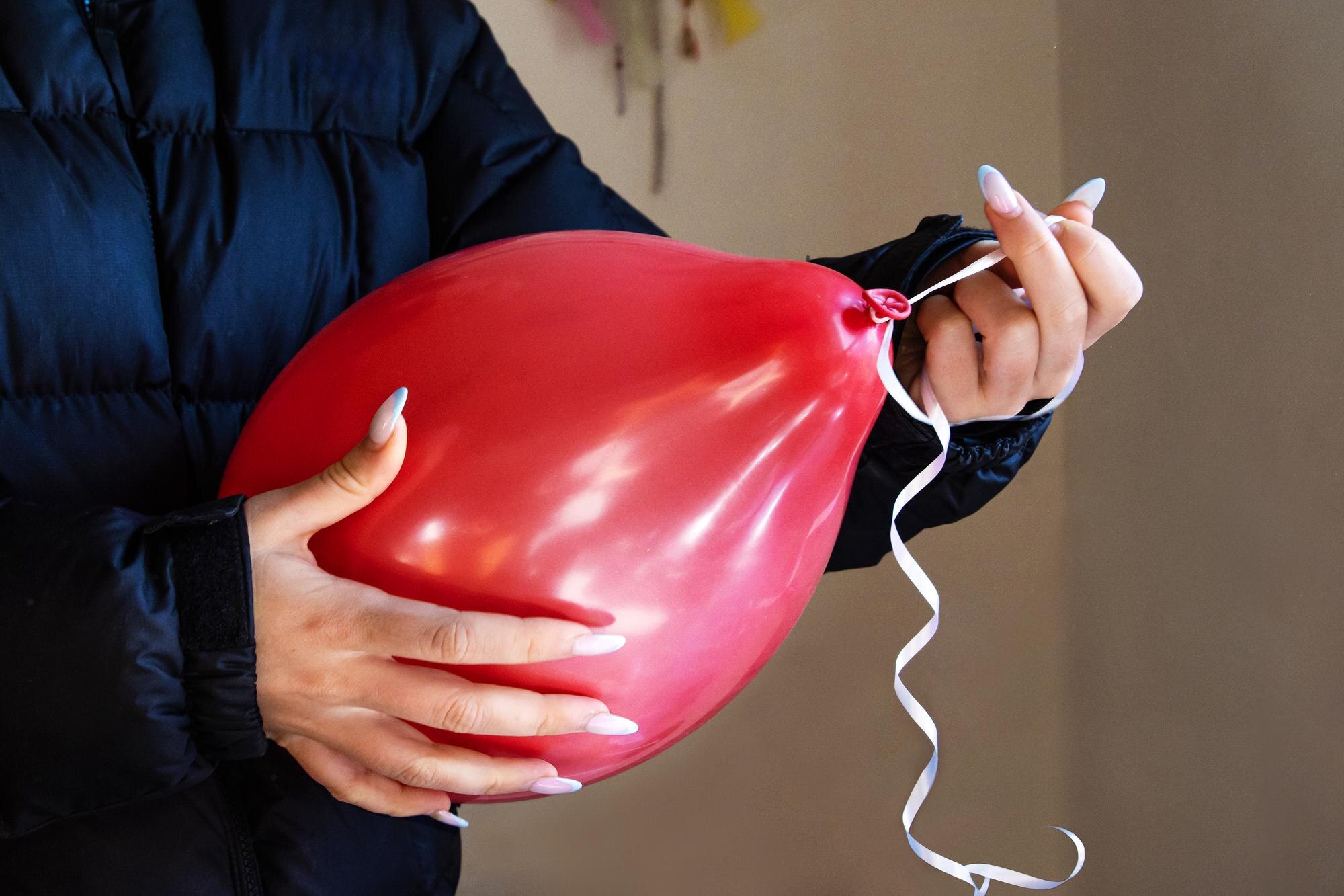 Zbliżenie rąk kobiety wiążącej wstążkę na czerwonym balonie do dekoracji imprezy Osoba trzymająca balon z kręconą wstążką podczas przygotowań do imprezy urodzinowej