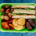 A nutritious lunch box featuring sandwiches, fresh fruit, and dried snacks, perfect for a balanced meal.