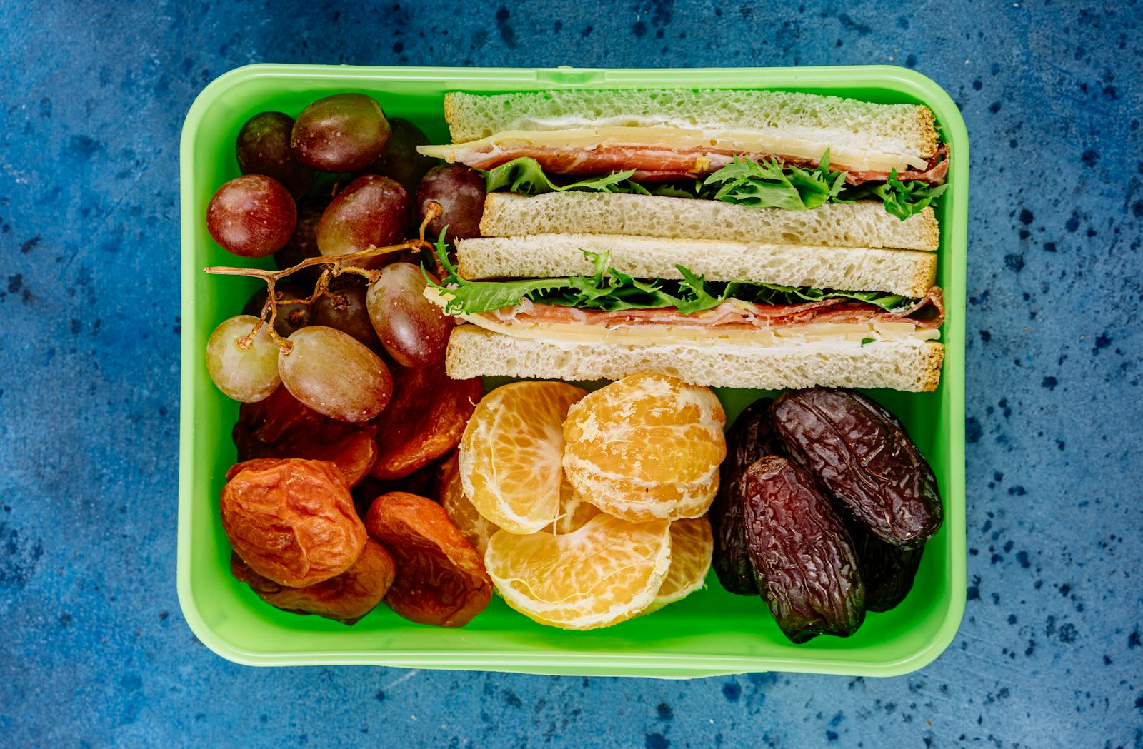 A nutritious lunch box featuring sandwiches, fresh fruit, and dried snacks, perfect for a balanced meal.